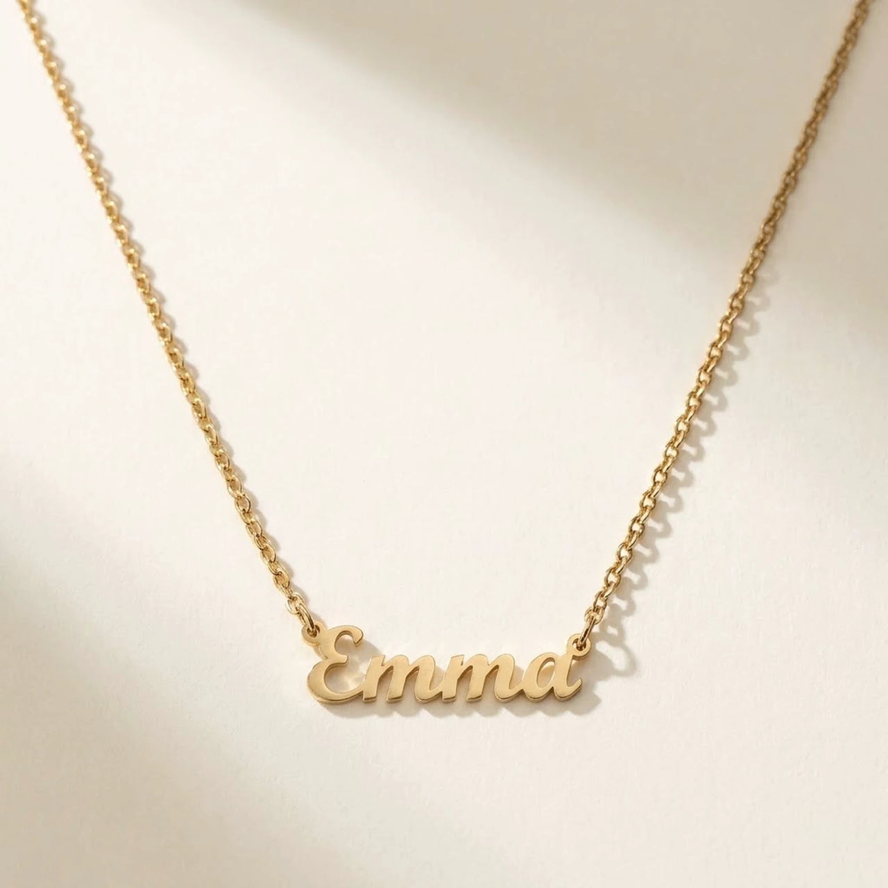 Minimalist Name Necklace in gold laid flat, the name Emma in cursive cut-metal script | SKU: minimalistnn-gold