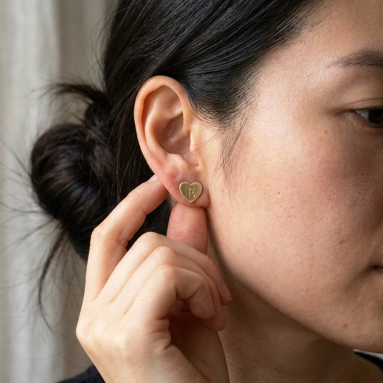 Heart Initial Stud Earrings in Gold held between the fingertips, scale reference | SKU: heart-initial-gold-a