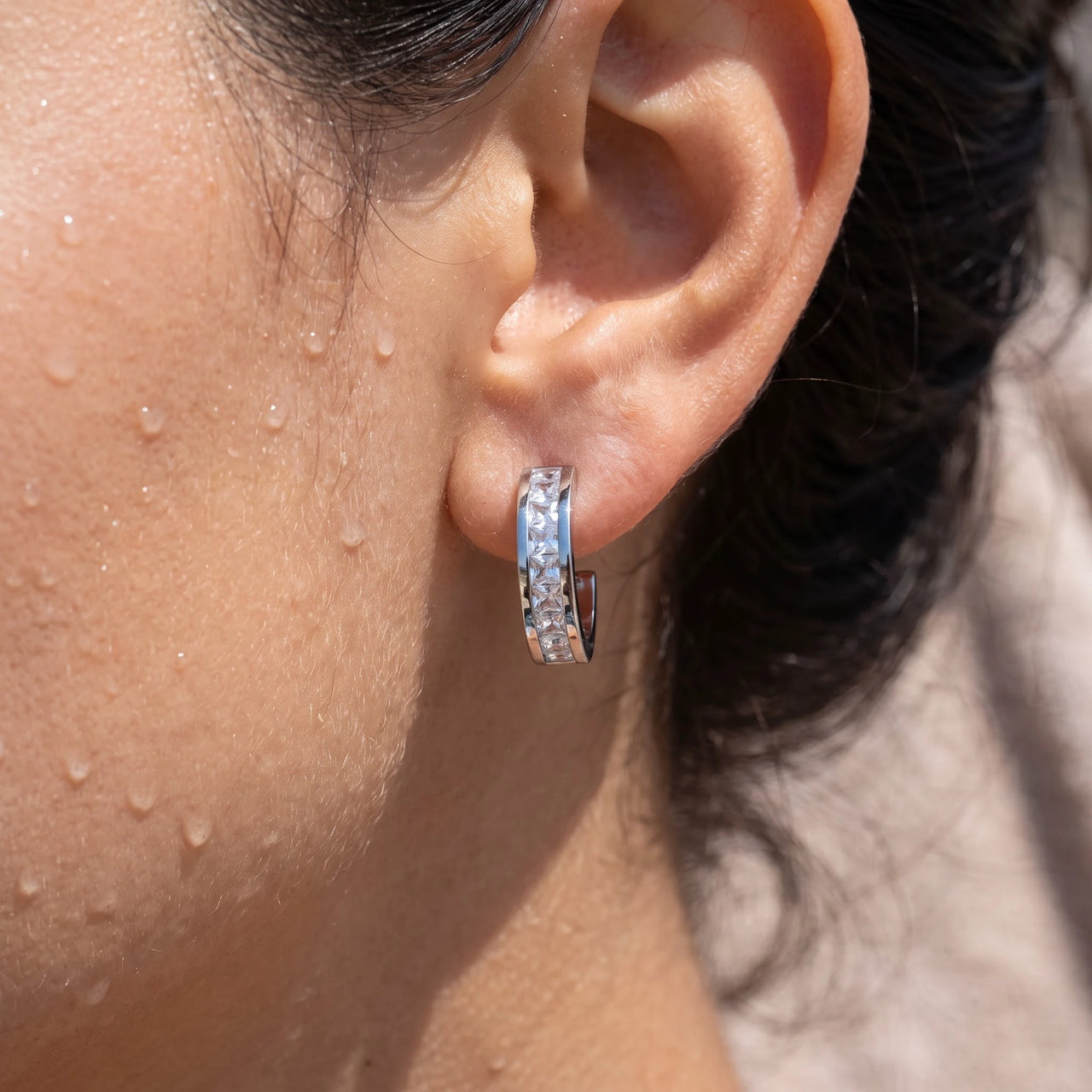 Close-up of the silver huggie hoop earrings worn on the skin | SKU: 22023999-rhodium