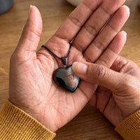 Thumbnail for Thumb warming the black heart pendant: the hidden photo appears under the thumb while the rest stays black | SKU: TPH-CHTN-BLACK-SMALL