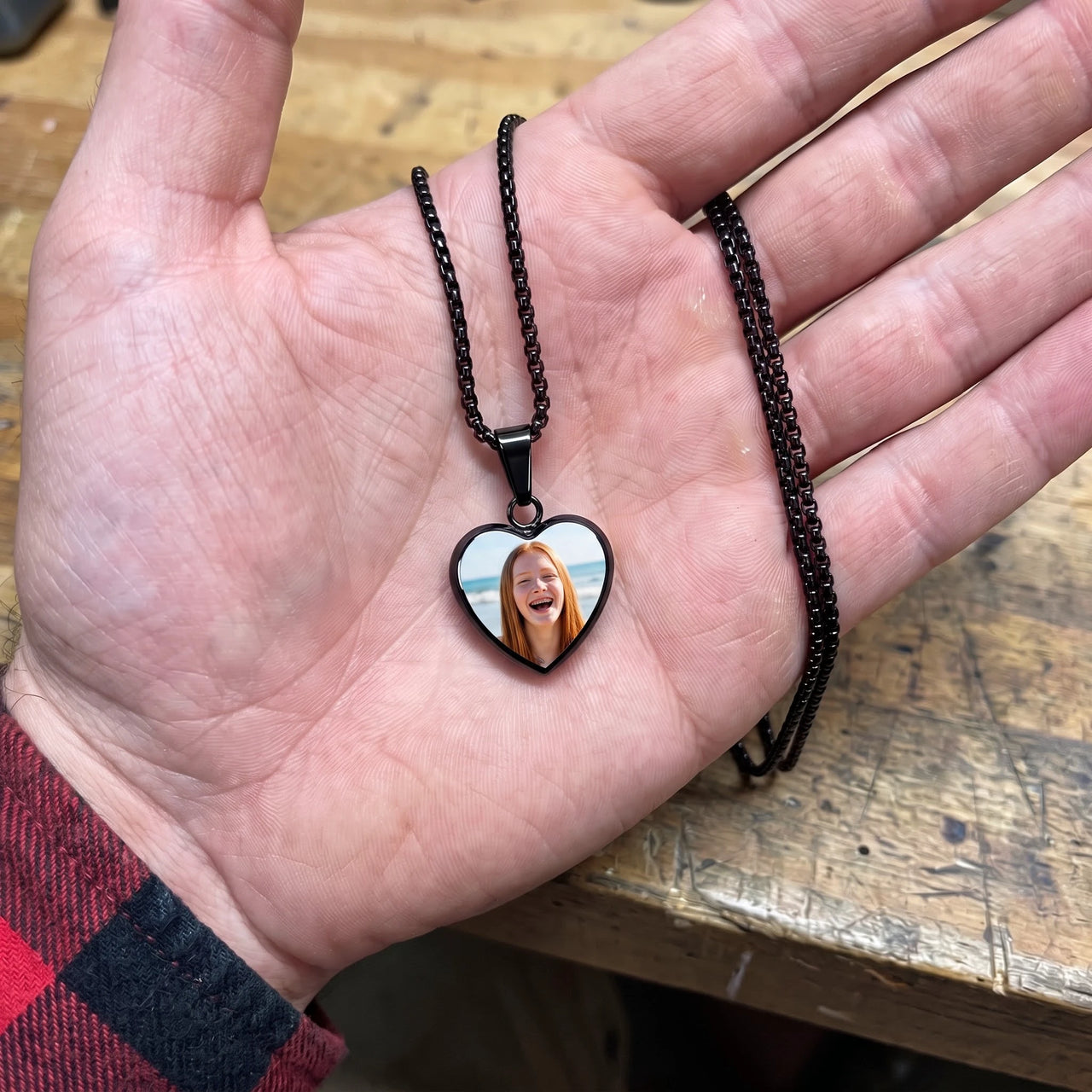 The black heart photo pendant in an open palm, showing its real small size | SKU: TPH-CHTN-BLACK-SMALL