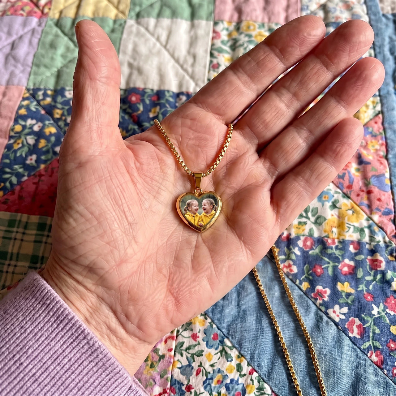 The gold heart photo pendant in an open palm over a quilt, showing its real small size | SKU: TPH-CHTN-GOLD-SMALL